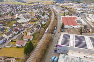 Train in a suburban landscape with residential buildings and industrial complexes, surrounded by