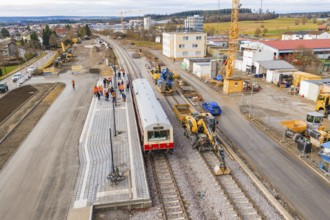 Train surrounded by workers and cranes at construction site, industrial buildings and vehicles in