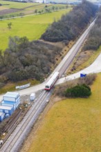 Train travels through a rural landscape with small infrastructures and surrounded by fields,