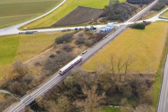 A train on rails crosses a rural landscape with fields and hills, historic event, first test run
