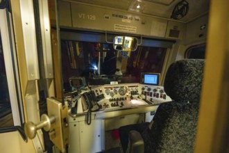 Interior view of a dark train driver's cab at night with illuminated control panel and technical
