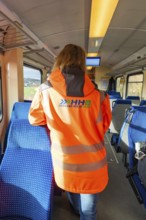 Person wearing safety clothing in the passenger area of a train, blue seat cover and looking