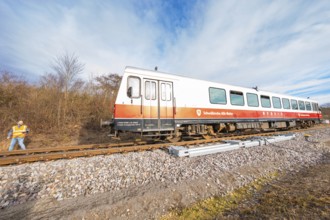 A train with a worker standing on rails next to it, with a landscape of trees in the background,