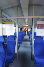 Interior of a train with blue seats and windows through which daylight enters, historic event,