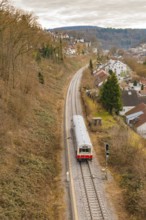 A single train travels on a railway line through a hilly residential area, historic event, first