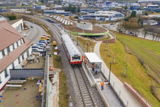 A train stops at a train station in an urban area, surrounded by buildings and parking lots,