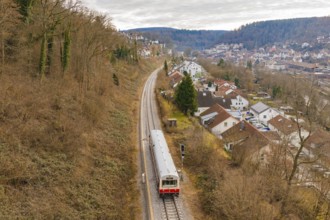 A train moves through a picturesque landscape with houses and hills in the background, historic