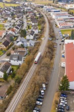A train travels through an urban area along railroad tracks, past residential and industrial