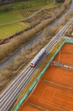 A train travels through rural landscape next to orange tennis courts on railroad tracks, historic