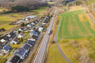 A train travels through a village, surrounded by fields and forests, along the railway tracks,