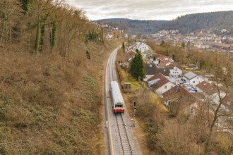 A train travels through an autumn landscape near a village with hills in the background, historic