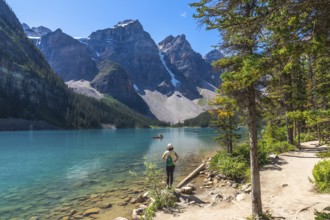 Female tourist standing on the shore of the turquoise moraine lake, admiring the canadian rockies