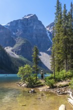 Female tourist walking along the scenic shores of turquoise moraine lake and enjoying the