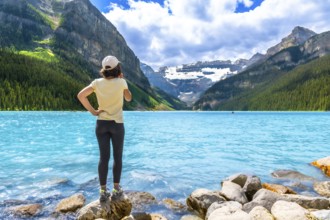 Tourist standing on rocks at the edge of vibrant turquoise waters of lake louise, admiring majestic