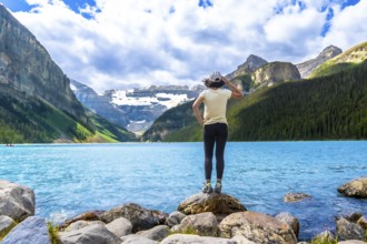 Tourist standing on rocks by the turquoise water of lake louise admires the surrounding canadian