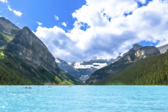 Canoes are paddling on a beautiful turquoise lake with surrounding mountains and glaciers in banff