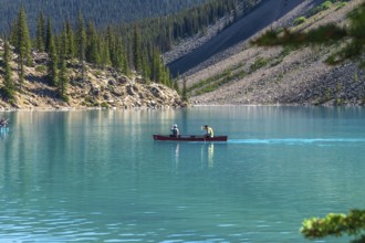 Two tourists paddling a red canoe on the turquoise waters of moraine lake in banff national park,