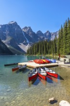 Colorful canoes are waiting at a wooden dock on the turquoise, pristine waters of moraine lake in