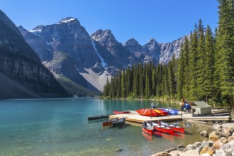 Colorful canoes tied to a wooden dock on turquoise waters of moraine lake, surrounded by the
