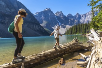 Mother and son balancing on a weathered log over turquoise waters of moraine lake, surrounded by