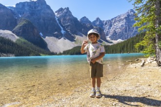 Young boy waving on the shore of moraine lake with the canadian rockies in the background, enjoying