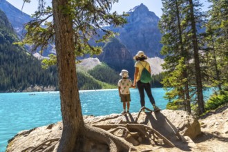 Mother and son holding hands on a rock by a tree, admiring the turquoise waters of moraine lake,