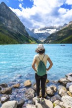 Young woman backpacker standing on rocks admiring stunning turquoise lake and surrounding mountains