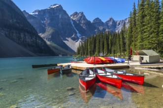 Reflecting red canoes in the turquoise waters of moraine lake, framed by snow capped mountains and