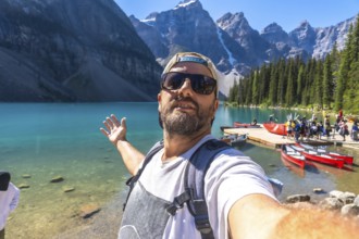 Backpacker taking a selfie with turquoise lake and canoes with the canadian rockies in the