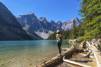 Female tourist standing on a log admiring the turquoise waters of moraine lake with the valley of