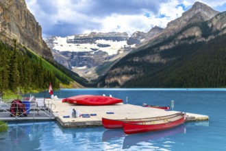 Red canoes are tied to a dock on the turquoise water of lake louise with a backdrop of snow capped