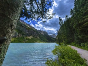 Sun shining through clouds illuminating turquoise waters of moraine lake and surrounding lush