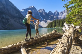 Mother and child balancing on a weathered log by the vibrant turquoise moraine lake, surrounded by