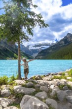 Young tourist balancing on rocks by a tree near the turquoise waters of lake louise, with snow