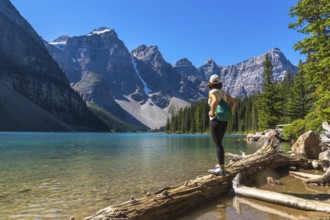 Female hiker standing on a log, admiring the stunning turquoise waters of moraine lake and the
