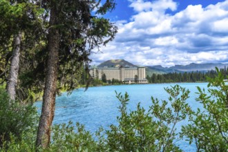 Lush vegetation framing turquoise waters of lake louise reflects a luxury hotel against stunning