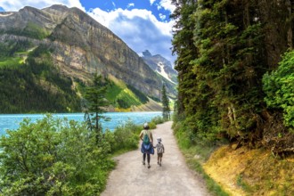 Mother and son walking along the scenic turquoise waters of lake louise with surrounding mountain