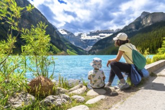 Mother and her child are sitting on the rocky shore of the turquoise lake louise, enjoying the
