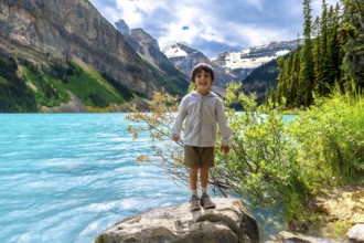 Happy child standing on a rock by the turquoise water of lake louise, enjoying the stunning scenery