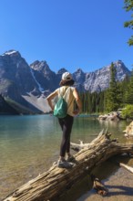 Female tourist standing on a log, admiring the turquoise waters of moraine lake, surrounded by the