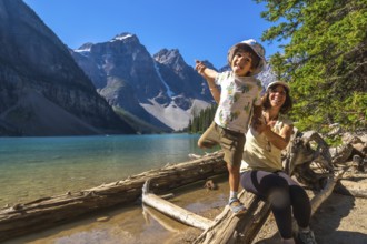 Mother and son are having fun while posing on a log by the turquoise waters of moraine lake,