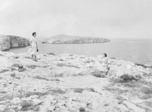 Two young woman at rocky coastal area with St Paul's Island in background, St Paul's Bay, Malta,
