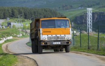 An orange truck is driving on a country road through a green hilly landscape, KamAZ-5511 truck,