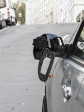 A car on the side of a steep residential street. The vehicle's left wing mirror is severely damaged