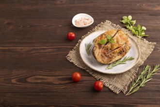 Fried Turkey Thigh with spices and rosemary on plate on brown wooden background and linen textile.