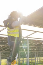 Man installing solar panel, wearing safety vest, with sun rays in the background, Energiewende,