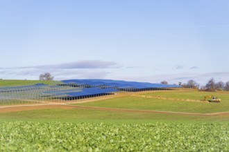 A tractor works in a field with installed solar panels under a blue sky, Energiewende, construction