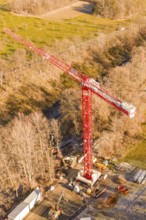 Red crane on a construction site, surrounded by autumnal forests and seen from the air,