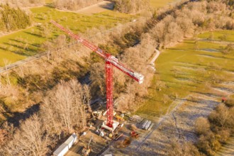 Red crane on construction site in autumn landscape with forests and meadows from a bird's eye view,