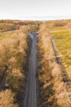 Aerial view of a train line through autumnal forests, parallel to a road, construction of the